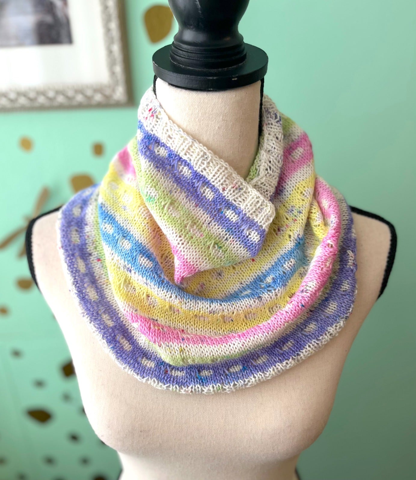 Egg Sighted Cowl draped over a manequin in pastel colors of purples, pinks, greens and beige  